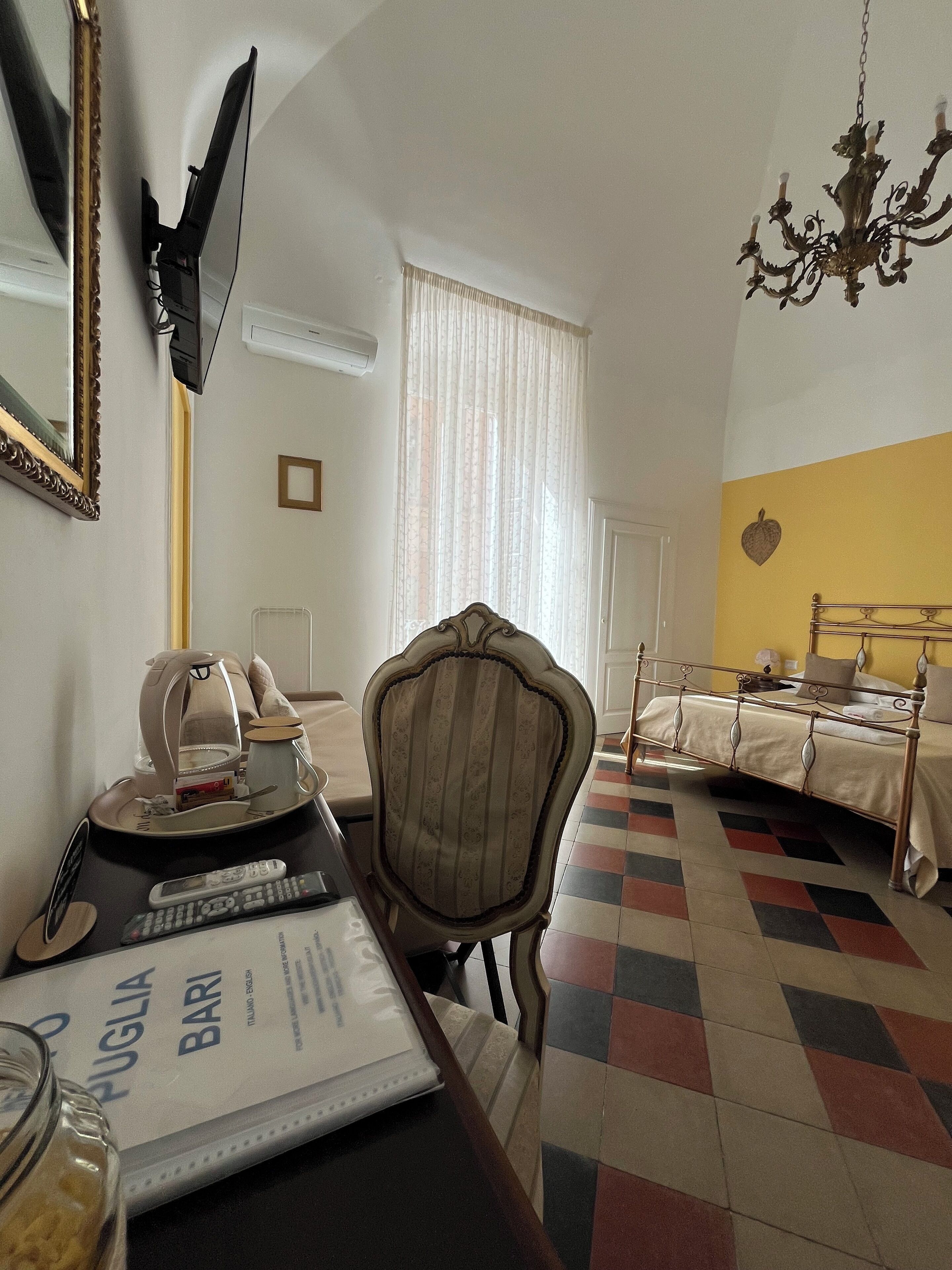 Quarto de hotel com uma cama, uma cadeira, uma mesa com um controle remoto, um cardápio e um espelho.