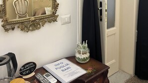 Una stanza con un grande specchio decorato, un settimino in legno con un libro, un vaso e un telecomando.