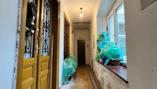 A hallway with a tiled floor, a door with a decorative metal grille, and a window with items covered in plastic. - Cozy Room in Apartment, Prime Locatio (Wien)