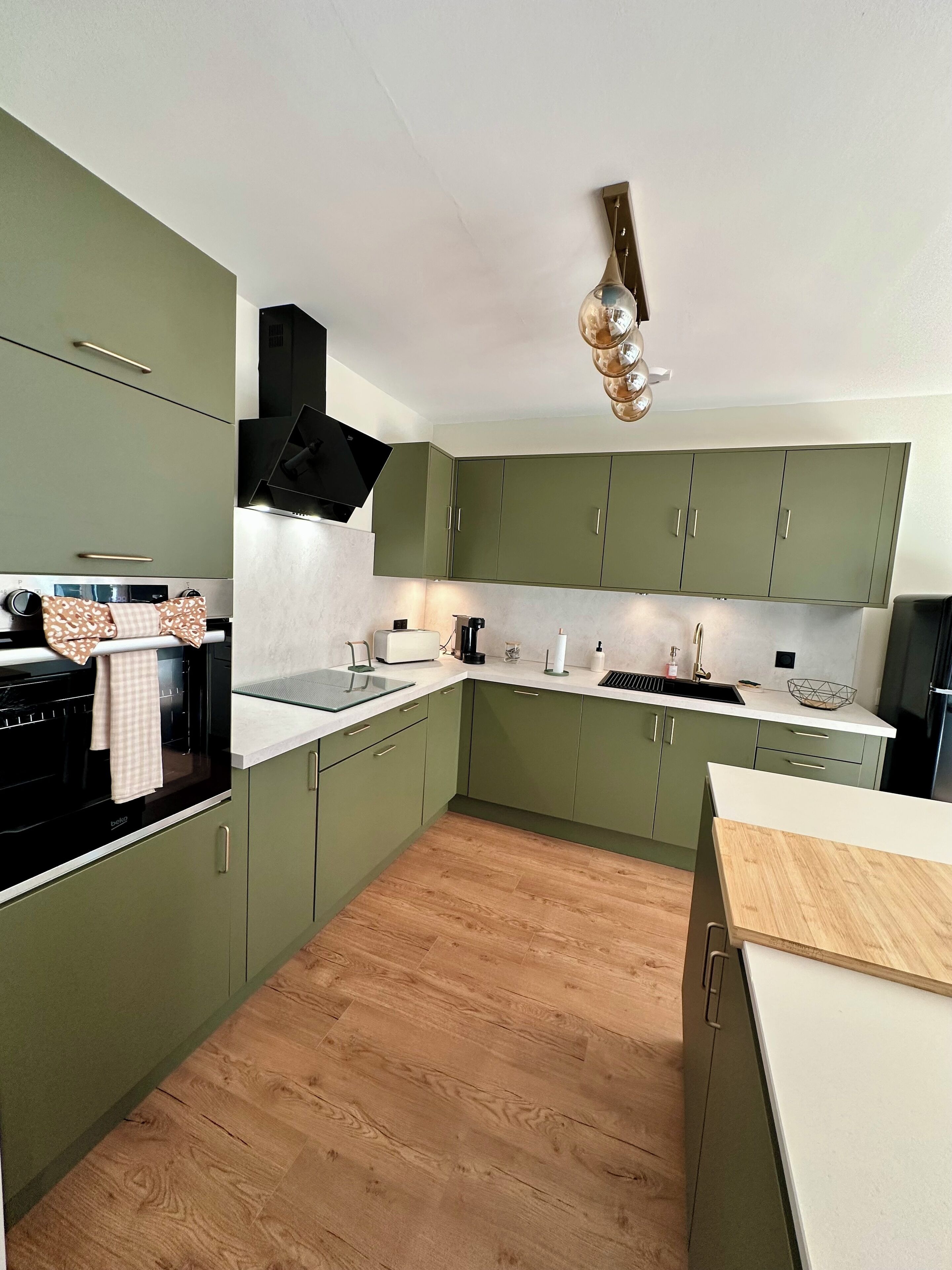 Une cuisine de taille réduite avec des meubles verts, une cuisinière noire et un plan de travail en bois.