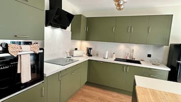 Une cuisine de taille réduite avec des meubles verts, une cuisinière noire et un plan de travail en bois.