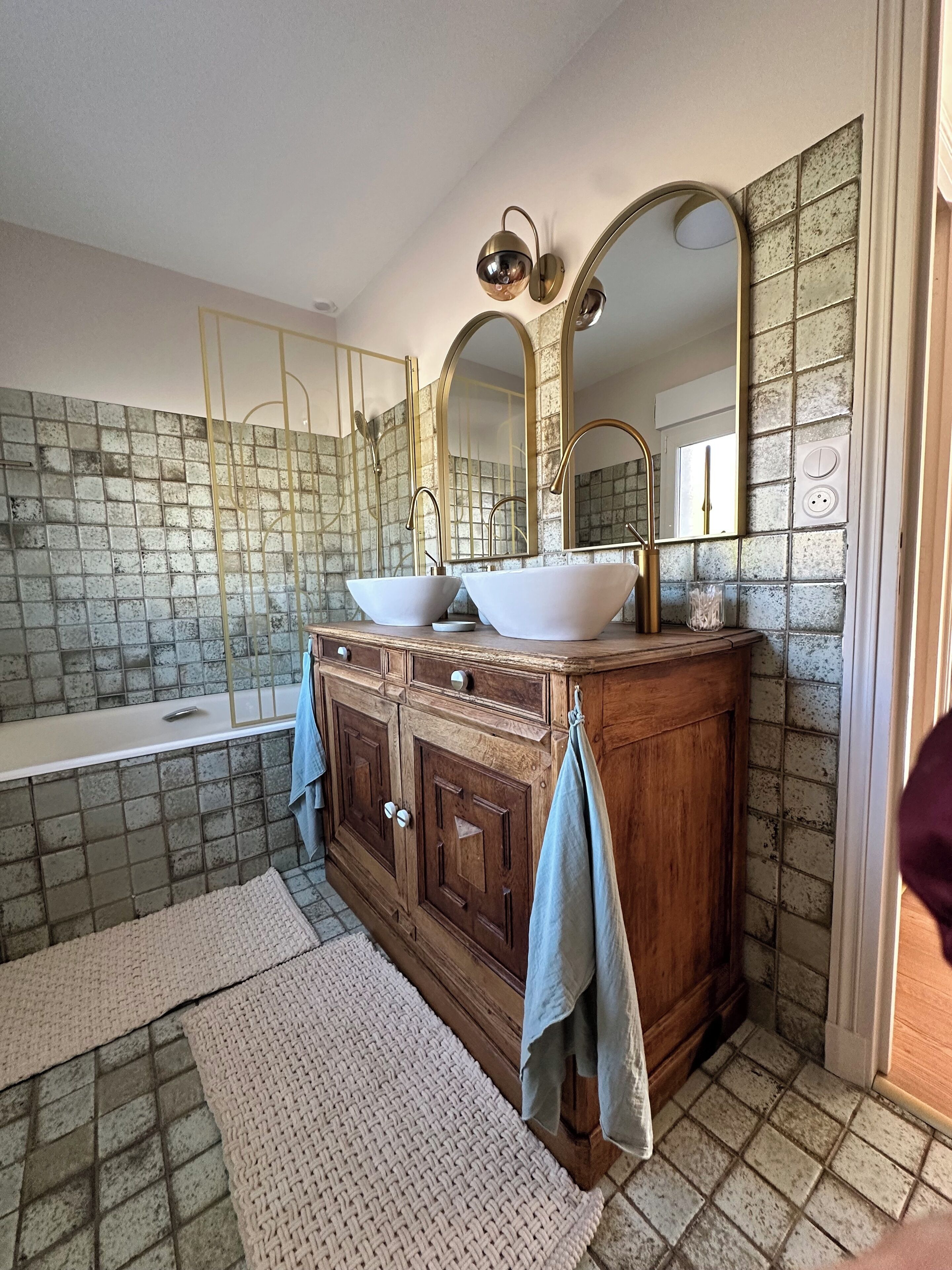 A bathroom with a wooden vanity, two vessel sinks, a large mirror, and a tiled backsplash.