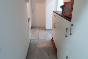 Ein schmaler Flur mit Fliesenboden, einer weißen Tür am Ende und einer Küchenzeile mit roten Geräten und Schränken.
