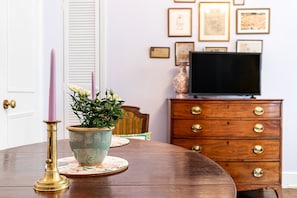 Ein Esstisch mit einem floralen Mittelstück, einer Kerze und einem Fernseher im Hintergrund.