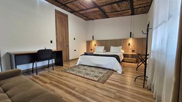 A modern bedroom with a wooden ceiling, a bed with white bedding, a desk with a chair, and a small sofa.