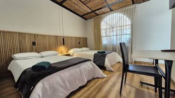 Quarto de hotel com duas camas, uma escrivaninha e uma cadeira.