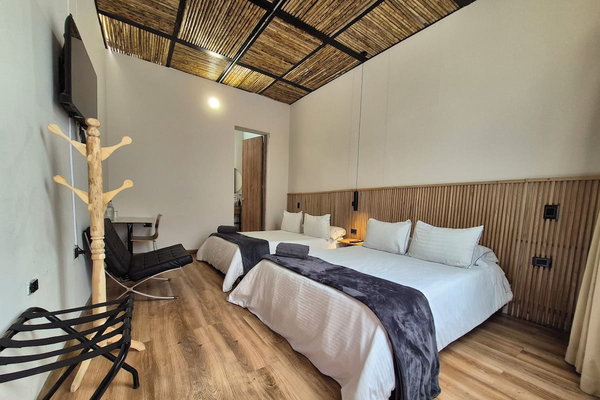 A modern hotel room with a large bed, a wooden headboard, a TV mounted on the wall, and a wooden ceiling.