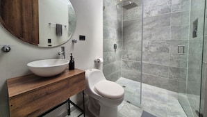 A modern bathroom with a round mirror, wooden vanity, white sink, and a glass-enclosed shower area. - Pepe's House Usaquén Bogotá -Small Hotel (Bogotá)