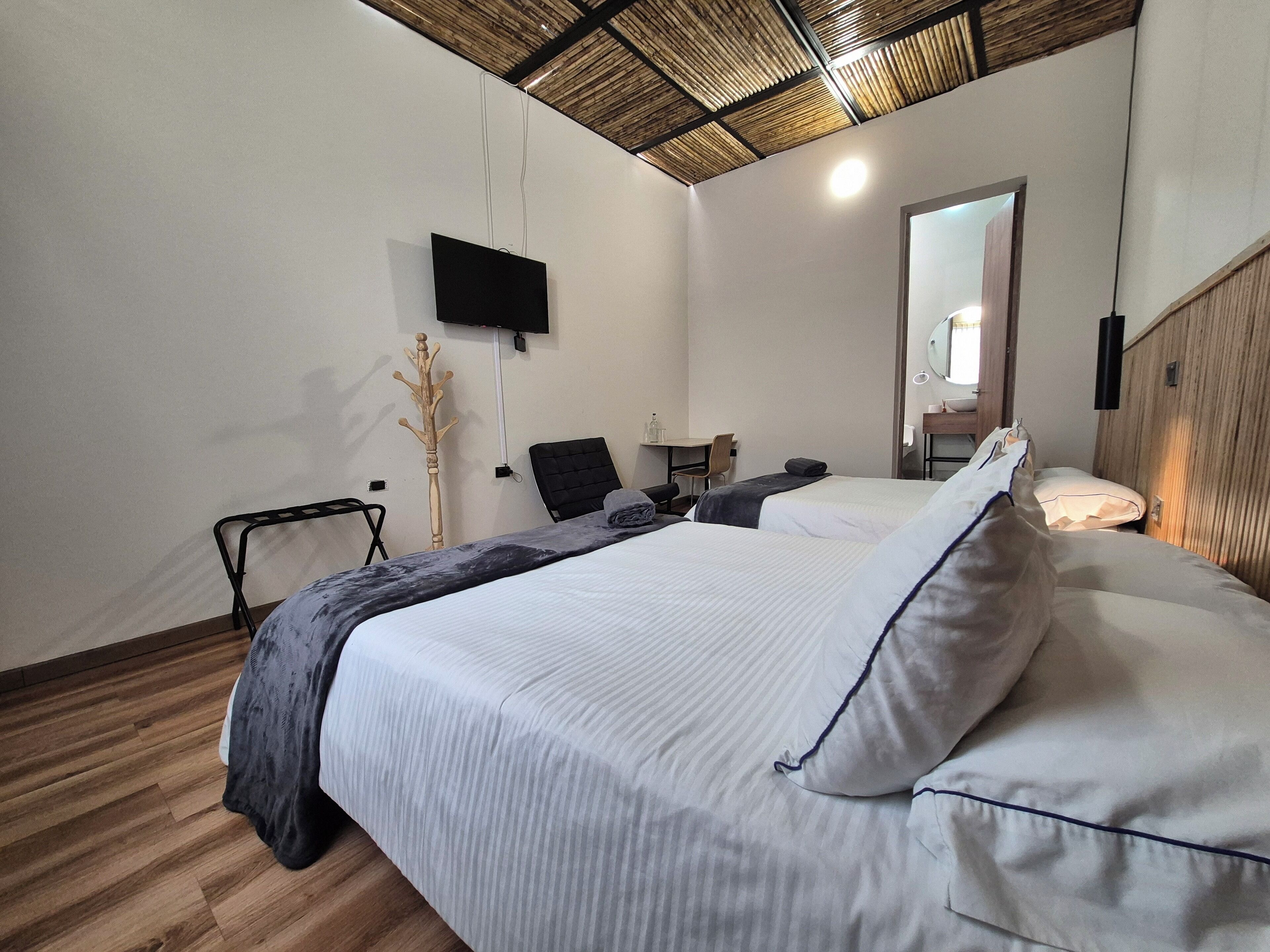 Habitación de hotel con una cama grande, un escritorio, una silla, un televisor instalado en la pared y techo de madera.