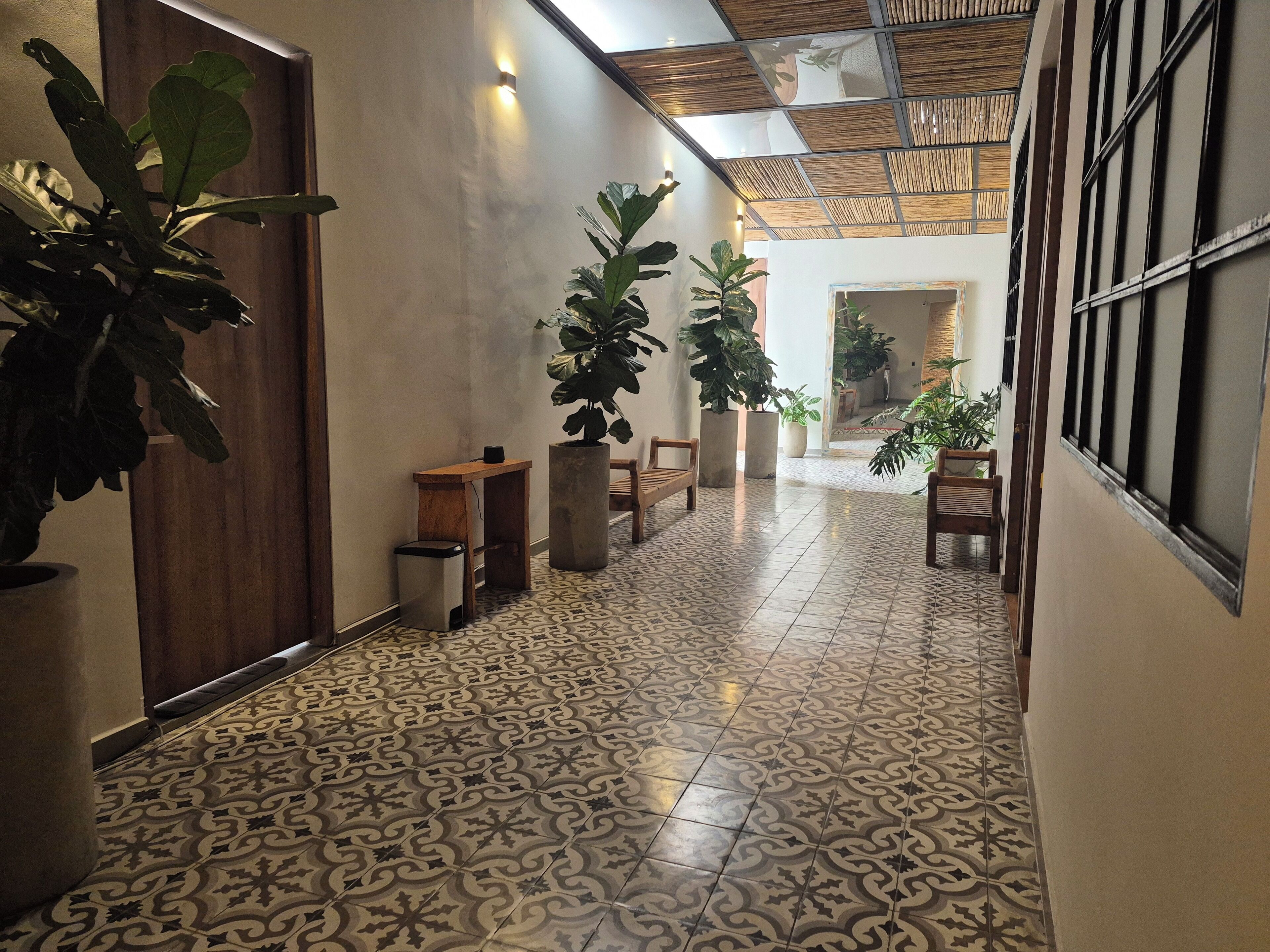 Un couloir avec des carreaux de sol à motifs, des bancs en bois et des plantes en pot.
