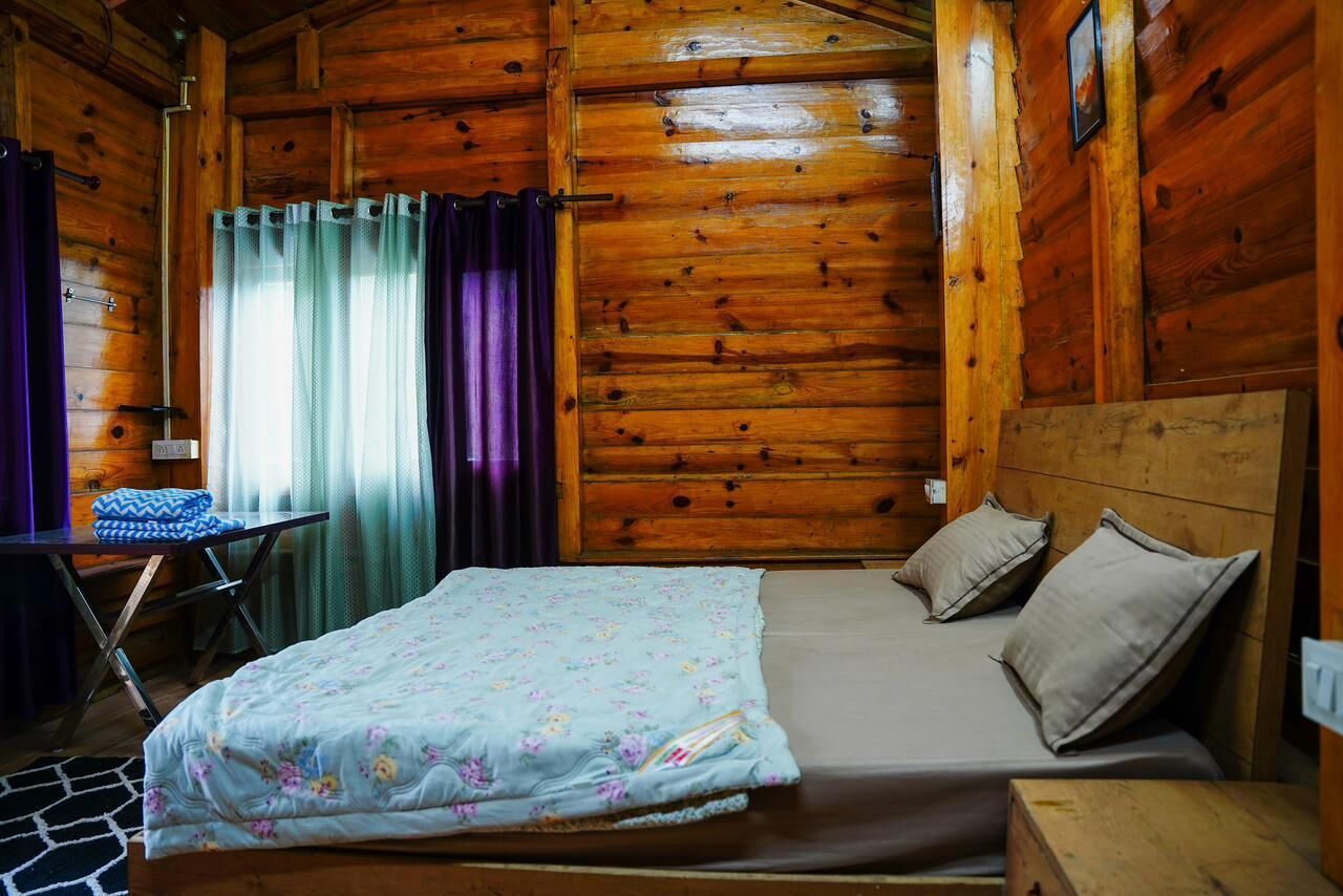 Una habitación tipo cabaña de madera con una cama, una mesita y una silla.