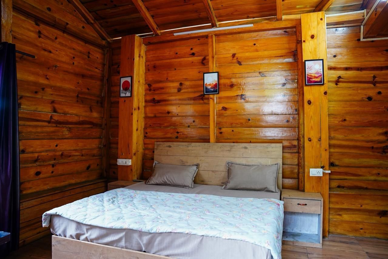 A wooden cabin bedroom with a bed, two pillows, a nightstand, and framed pictures on the walls.