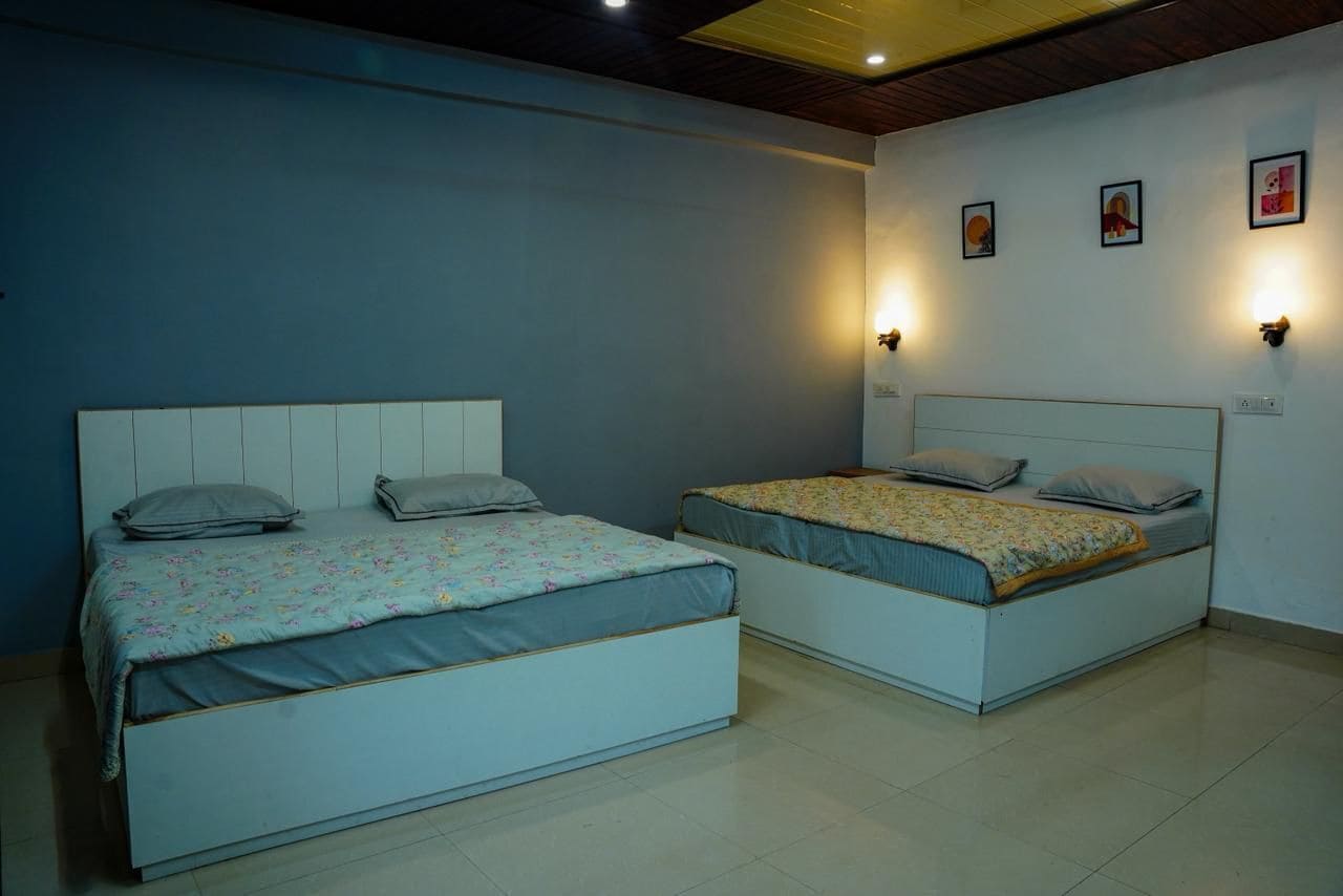 A bedroom with two beds, each with a headboard, pillows, and a blanket. There are wall-mounted lights and a ceiling light.