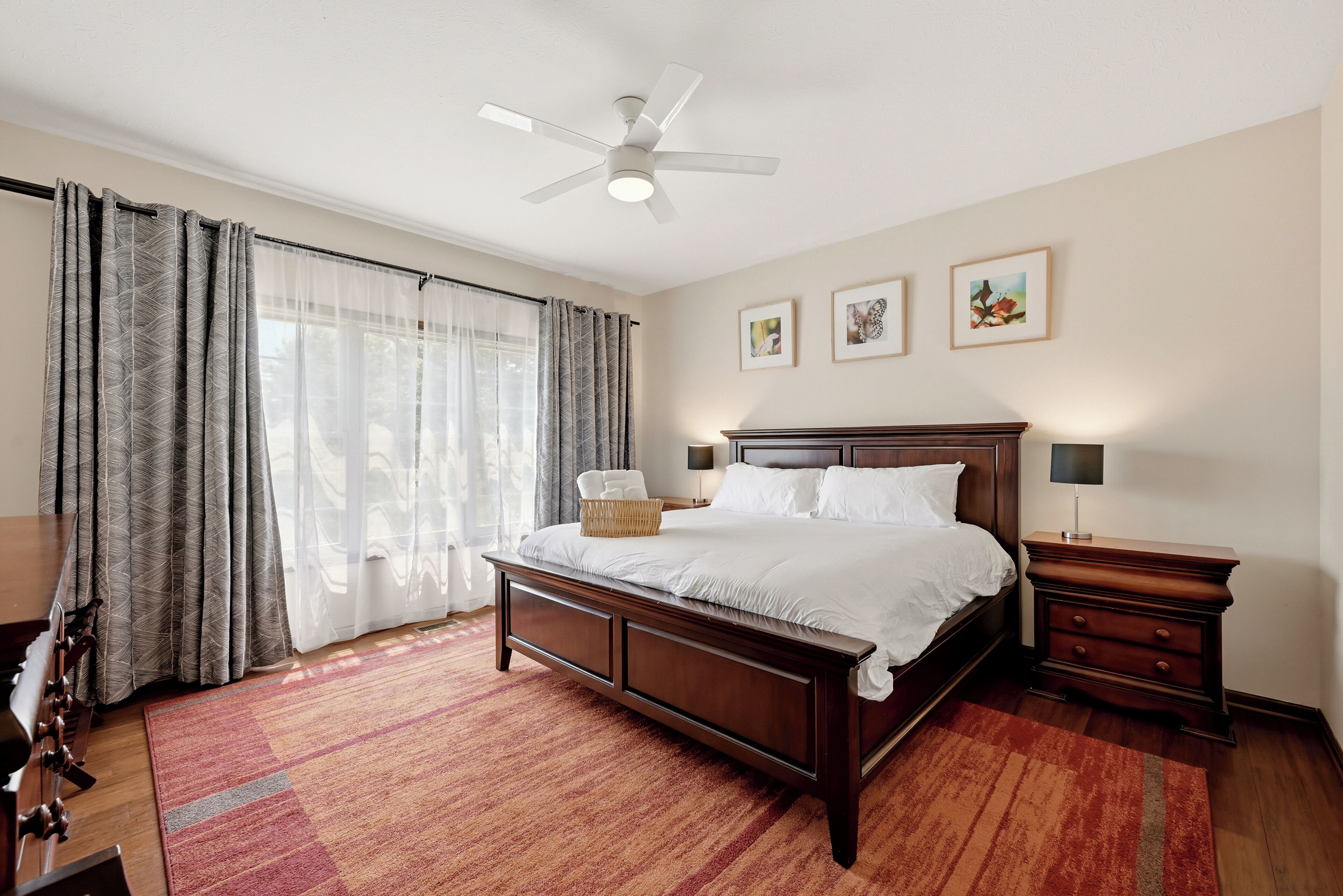 A bedroom with a bed, a nightstand, a lamp, a ceiling fan, and a window with curtains.