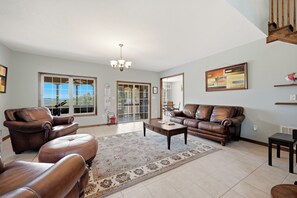 A spacious living room with leather furniture, a chandelier, and large windows.
