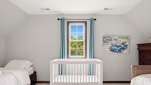 A room with a crib, a bed, a dresser, a window with curtains, and a painting on the wall.