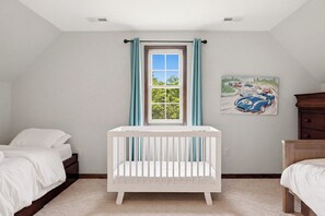 A room with a crib, a bed, a dresser, a window with curtains, and a painting on the wall.