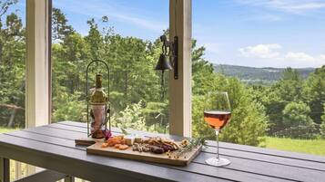 A wooden table with a charcuterie board, a bottle, and a wine glass, set against a scenic outdoor view.