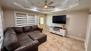 Ein Wohnzimmer mit einem braunen Ledersofa, einem Flachbildfernseher auf einer weißen Unterhaltungsanlage und einem Deckenventilator.