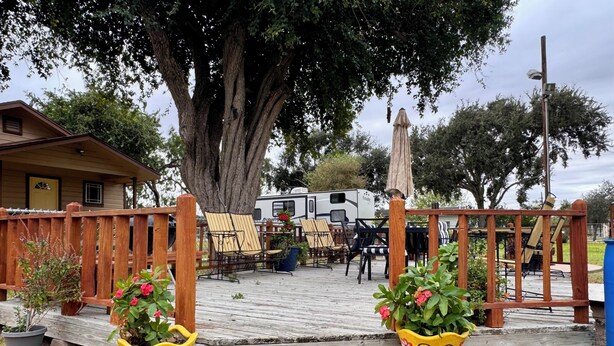 Eine Holzterrasse mit Sitzgelegenheiten im Freien, einem überdachten Bereich und einem Wohnmobil im Hintergrund.
