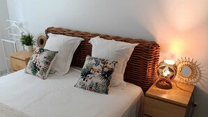 Cama bem arrumada com lençóis brancos, duas almofadas iguais, cabeceira de palha e duas mesas de cabeceira com abajures.