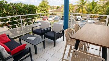 A balcony with a table and chairs, a view of parked cars and palm trees, and a blue pillar.