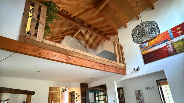 Ein geräumiger Wohnbereich im Loft-Stil mit hohen Decken, freiliegenden Holzbalken, einem großen Couchtisch, einer schwarzen Ledersofa und einem farbenfrohen abstrakten Gemälde.