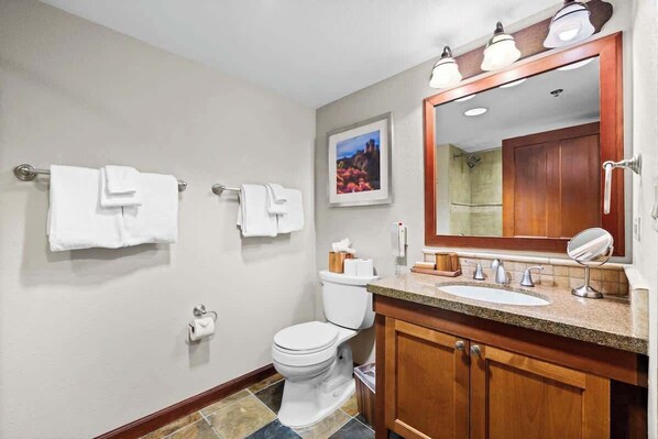 Une salle de bain avec des toilettes, un lavabo et un miroir. Il y a des serviettes accrochées au mur et un tableau au-dessus des toilettes.