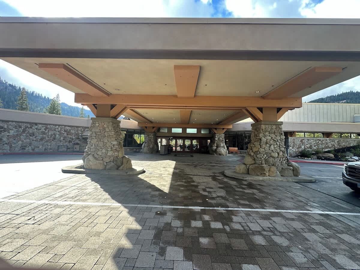 A covered outdoor area with stone pillars and a tiled floor, leading to a building entrance.