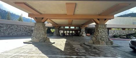 A covered outdoor area with stone pillars and a tiled floor, leading to a building entrance.
