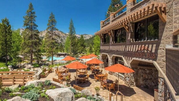 Un espace patio avec des sièges d’extérieur et des parasols, une piscine et un bâtiment à la façade en pierre.