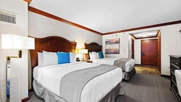 Quarto de hotel com duas camas, um encabedal de madeira, uma escrivaninha e uma porta.