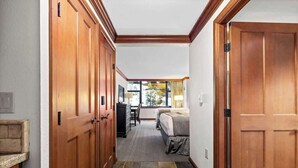 Un couloir avec des portes en bois menant à une chambre à coucher équipée d’un lit et d’un bureau.