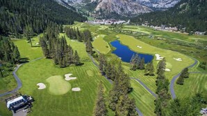 Un campo de golf con un lago, rodeado de montañas y bosques densos.