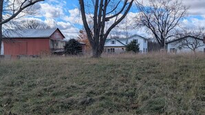 Ländliche Landschaft mit einem roten Bauernhaus, einem weißen Haus und einem großen Baum im Vordergrund.