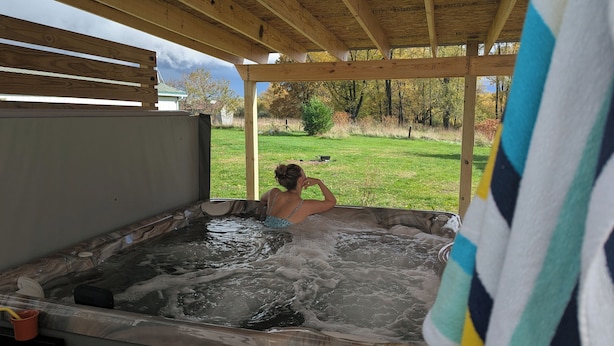 Eine Person entspannt sich in einem Whirlpool mit Blick auf einen Rasen und Bäume.