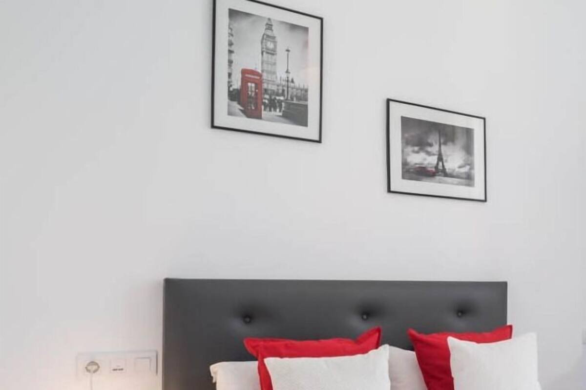 Habitación de hotel ordenada con cama, almohadas, mesita de noche y velador.