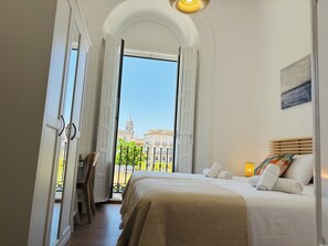 Ett hotellrum med en säng, utsikt över byggnader och en balkong.