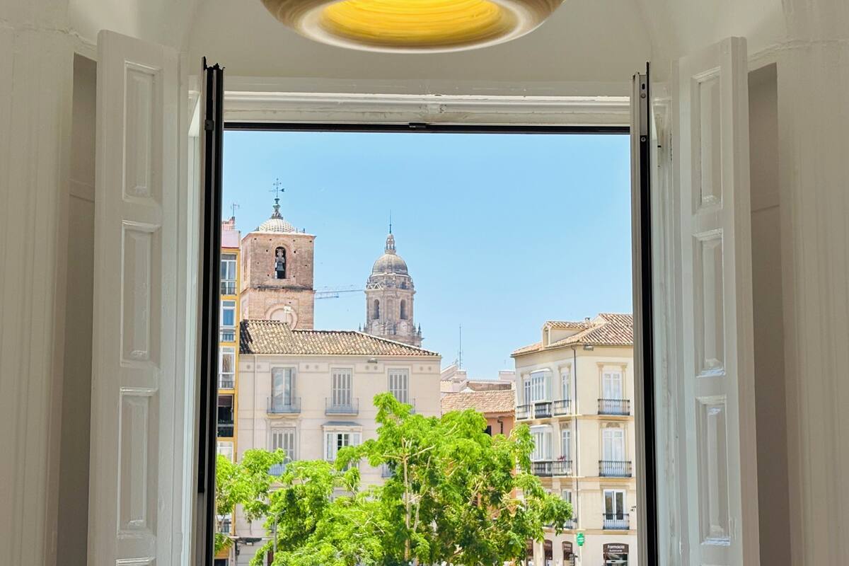 Una puerta abierta que muestra una vista de un edificio con una torre de campanas y una cúpula, rodeado de árboles y otros edificios.