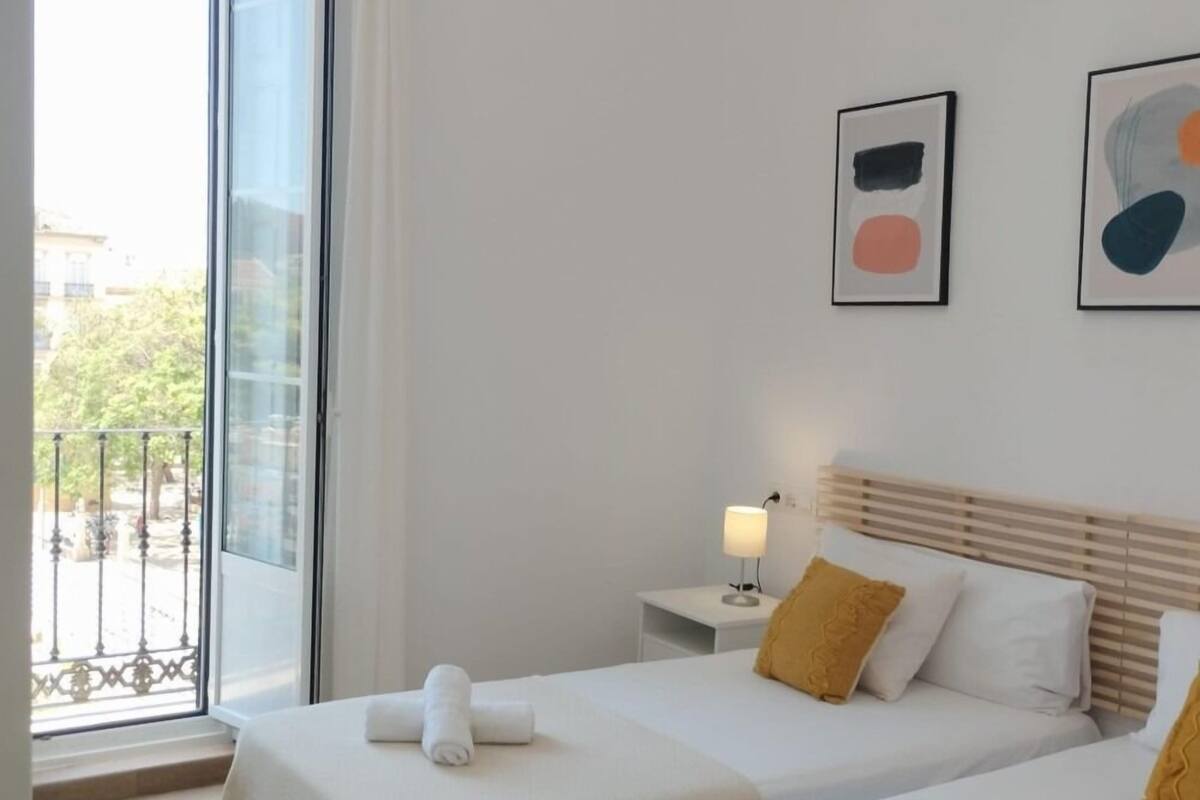 Habitación de hotel con dos camas, una mesita de noche con lámpara y una obra de arte en la pared.