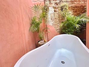 Eine weiße Badewanne in einem beengten Raum mit einer rosafarbenen Wand und einer rustikalen Ziegelwand im Hintergrund.