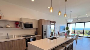 Uma cozinha moderna com ilha central, eletrodomésticos de aço inoxidável e iluminação pendente.