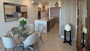 Cozinha moderna com ilha central, área de jantar com mesa de vidro e um painel decorativo de madeira à direita.