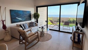 Uma sala de estar moderna com um sofá branco, uma mesa de centro de vidro e vista para o oceano através de grandes portas de correr.