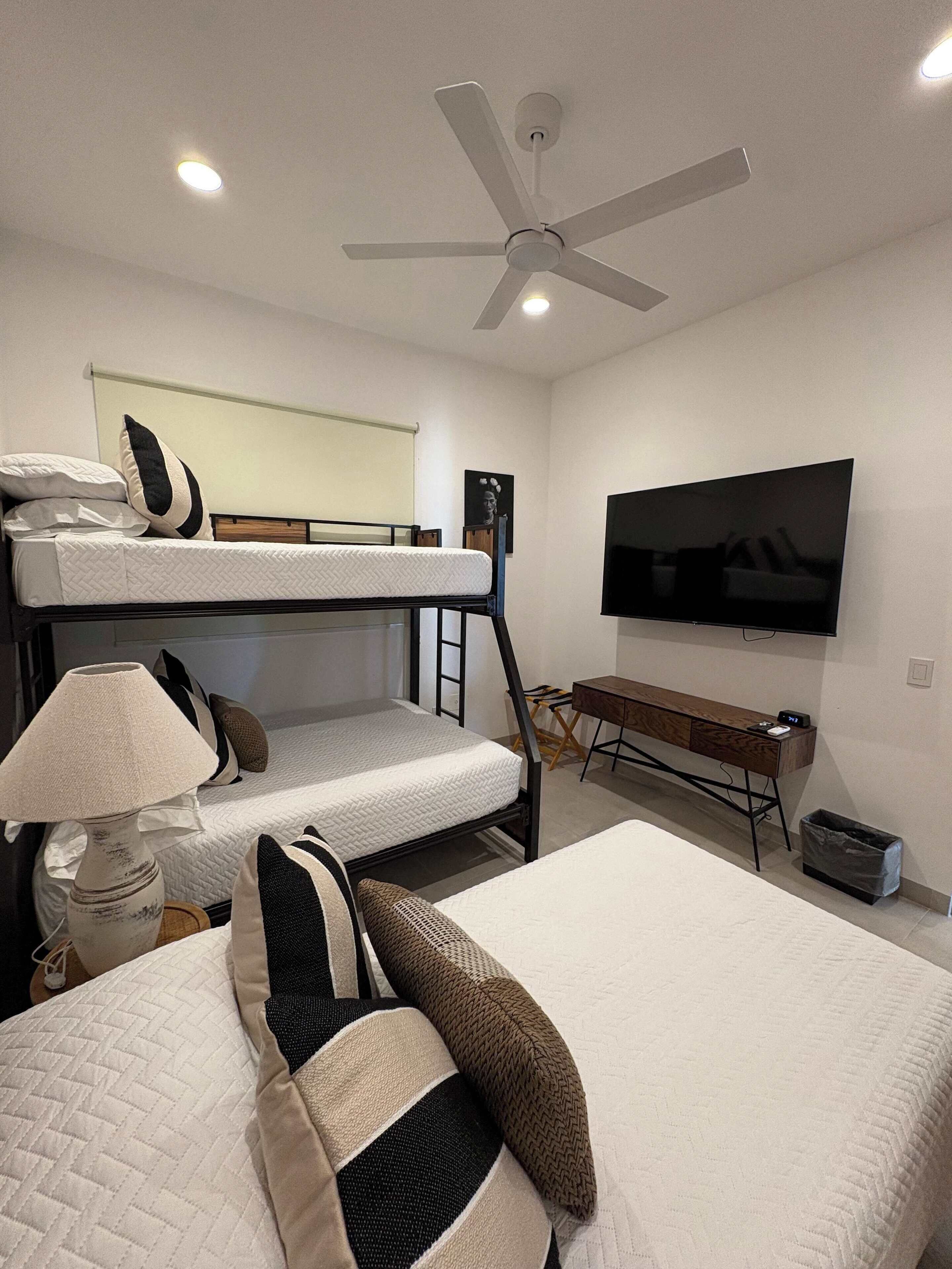 A hotel room with bunk beds, a desk, a television, and a ceiling fan.