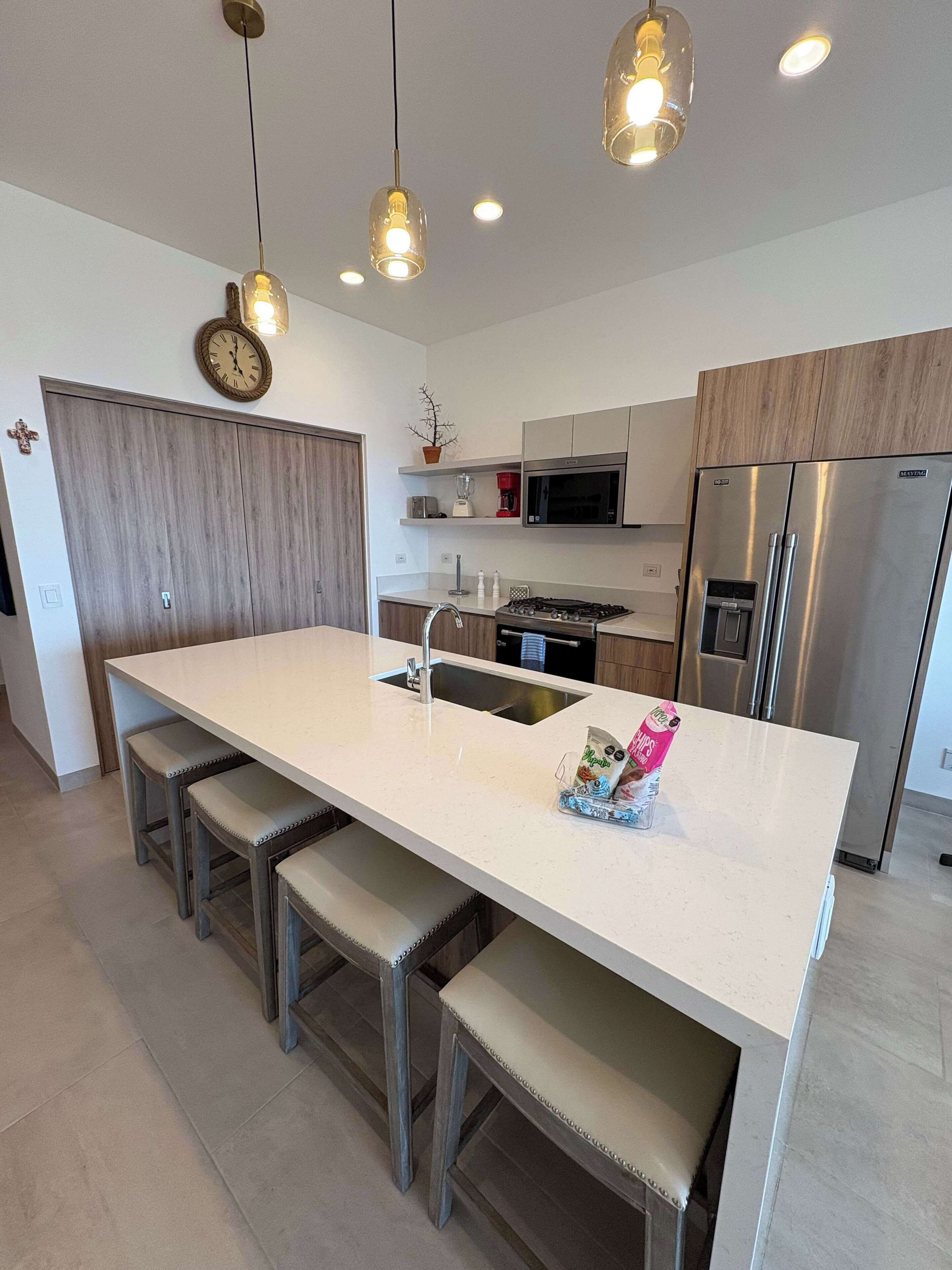 A modern kitchen with a central island, stainless steel appliances, and pendant lighting.