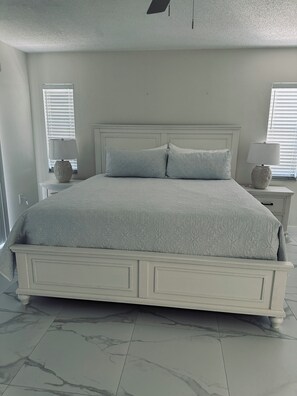 A bedroom with a large bed, two bedside tables, and a window with blinds. - Charming Villa in peaceful community minutes to Siesta Key (Sarasota)