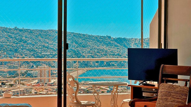 A balcony with a city view, a television, and a chair. - Ocean Front House 84 (Valparaíso)