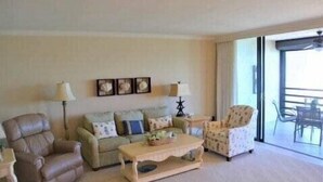 A living room with a sofa, two armchairs, a coffee table, and a lamp. There are wall art pieces above the sofa and a window with a view. - Great views of Marco River from 5th Floor condo (Marco Island)