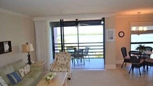 A living room with a sofa, a coffee table, and a dining area with chairs and a table. There is a large window with a view of the outdoors. - Great views of Marco River from 5th Floor condo (Marco Island)